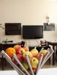 Wnętrze Domu Pomocy Społecznej. Na pierwszym planie kosz z jabłkami, stojący na stole. W tle telewizor wiszący na kremowej ścianie. Wzdłuż ściany, pod telewizorem, meble w kolorze ciemnobrązowym